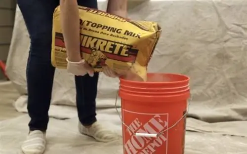 Руки в перчатках наливают смесь Quikrete Sand/Topping Mix в оранжевое ведро Home Depot