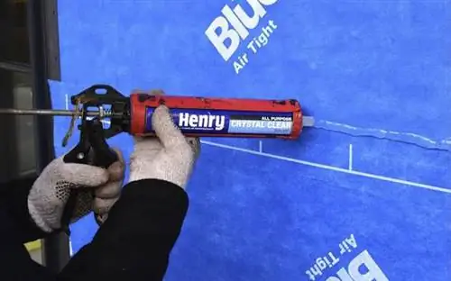 Рабочий наносит прозрачный универсальный пластырь Henry 212 на синюю строительную поверхность.