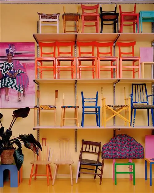 Yinka Ilori изучает желтую стену с дизайнерскими стульями Yinka Ilori изучает желтую стену с дизайнерскими стульями
