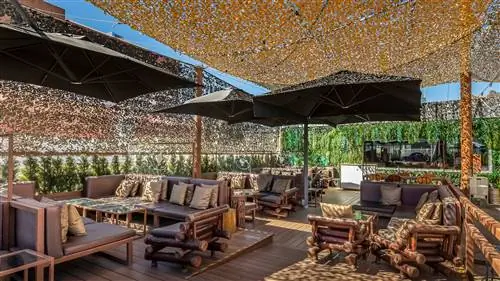 Изображение террасы ресторана с деревянными полами, ротанговыми и деревянными диванами и стенами из растительности