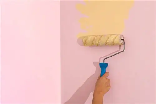 Обрезанная женщина вручную красит стену валиком, нанося желтую краску на розовую стену
