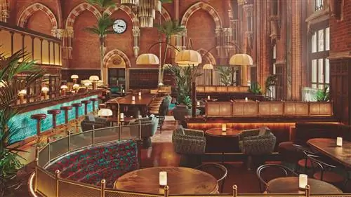 Просторный бар для afterwork с разными зонами с пальмами на стенах в темных и коричневых тонах с хлопковыми тканями…