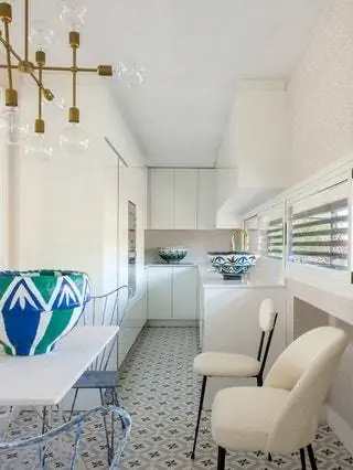 На кухне с белой лакированной мебелью от Aries и кафельным полом от Azulejos Peña французский стол с деревянными ножками…