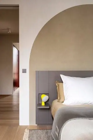 кровать с серым изголовьем, белой подушкой и желтой лампой