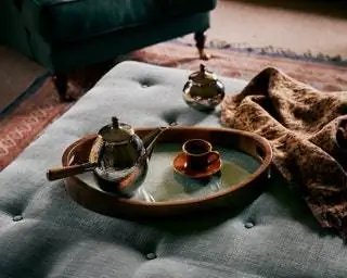 На деревянном диване-подносе и стеклянной сахарнице с чеканной керамической чашкой и льняным покрывалом все от Zara Home