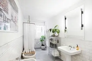 В ванной комнате с гладким цементным полом и облицовкой из белой плитки есть раковина на пьедестале,…