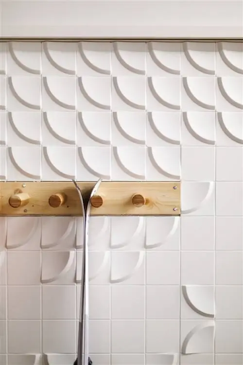 белая рельефная плитка с вешалкой из светлого дерева и лыжами