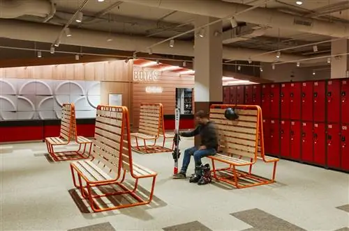 Раздевалка с деревянными скамейками с оранжевой металлической конструкцией, красными шкафчиками и большой белой плиткой на стенах…