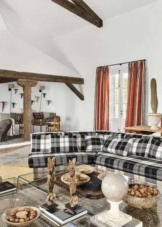 В углу гостиной диван с льняной шотландкой Playful Plaid от Dedar и стеклянный стол с ножками, которые…